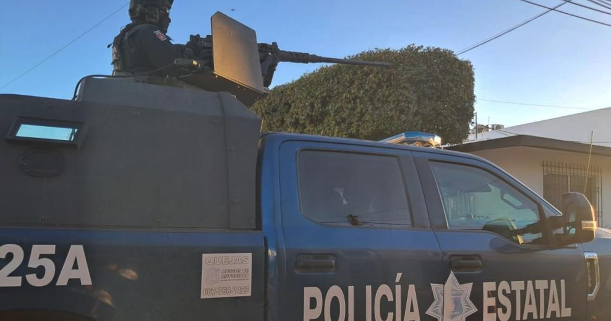 Vehículo de policía estatal con artillería en Culiacán, agente armado en la parte superior, cielo despejado y casas de fondo.