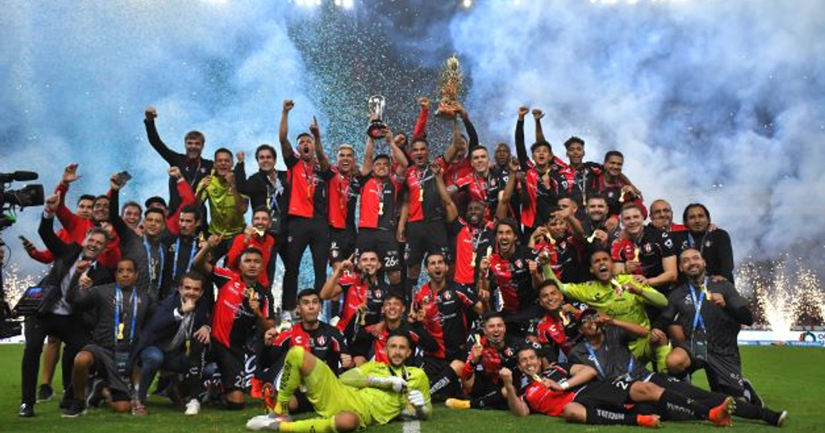 Jugadores del Atlas celebrando con trofeos y medallas en el Estadio Jalisco, rodeados de fuegos artificiales.