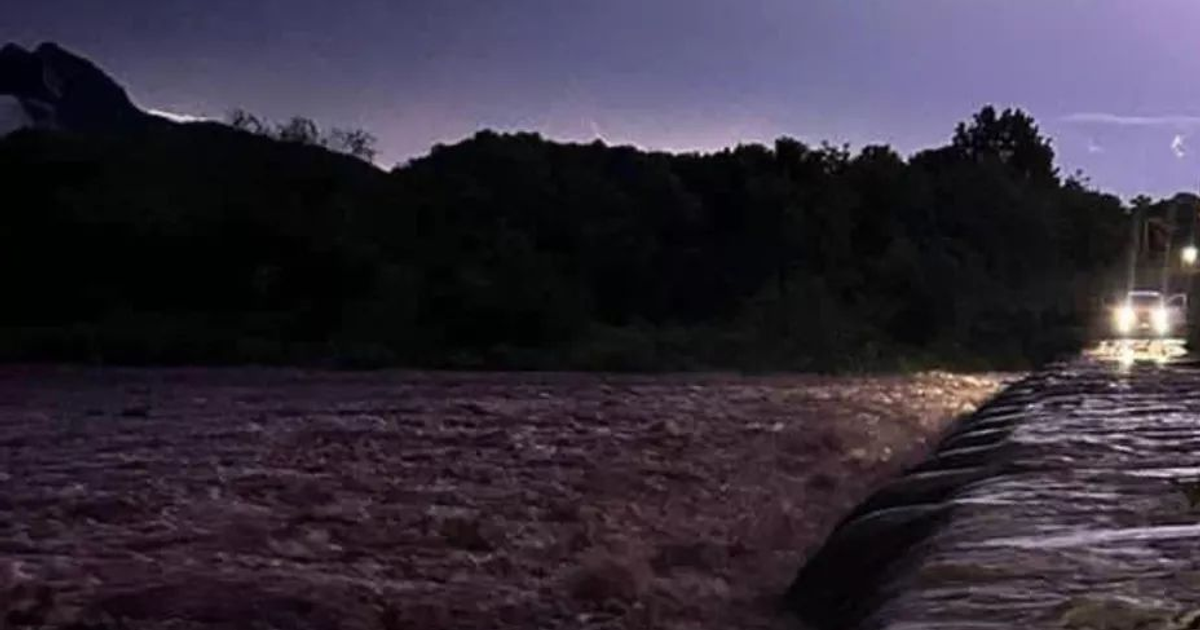 Río desbordado en Sinaloa con vehículo cerca, bajo un cielo tormentoso.