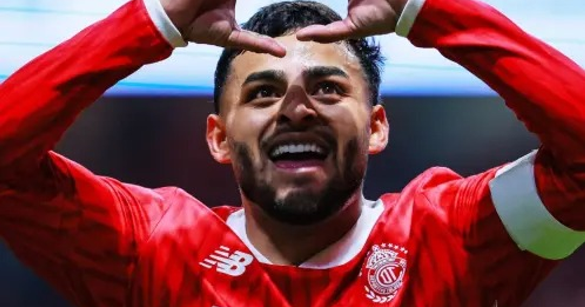 Jugador de fútbol con camiseta roja celebrando un gol con expresión emocionada y gesto de manos durante el partido Cruz Azul vs. Toluca.