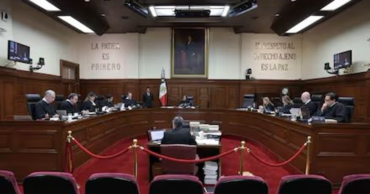 Jueces en una sala de tribunal con documentos y computadoras, retrato y bandera al fondo, frases en la pared sobre la paz y el respeto.