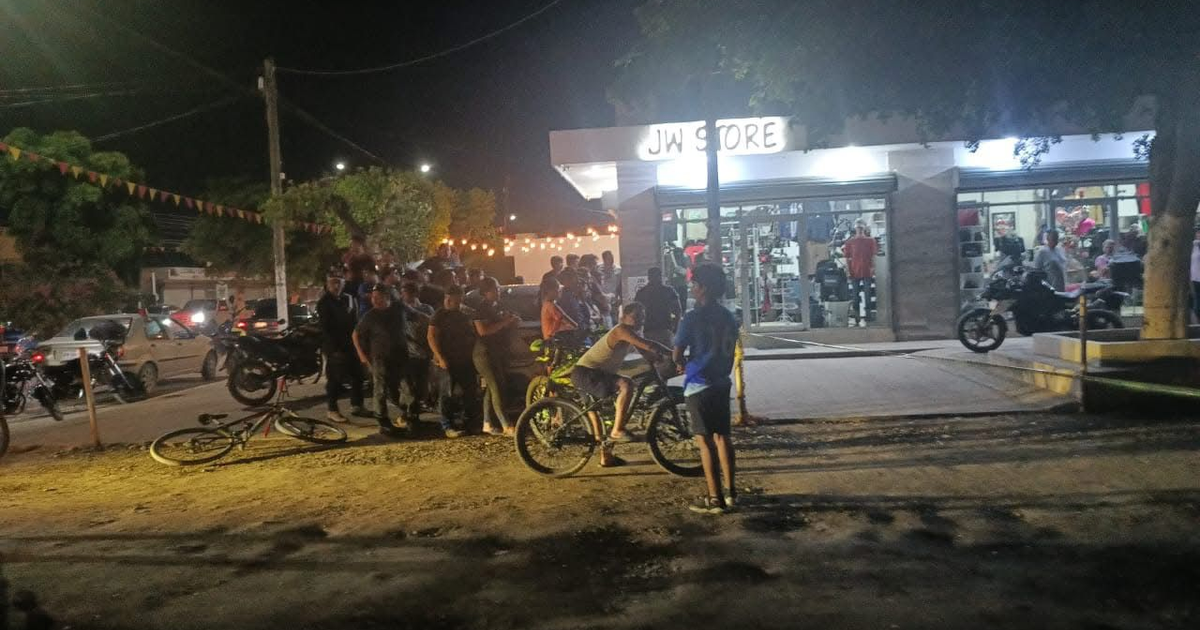 Grupo de personas reunidas frente a JW STORE en una calle nocturna de Aguaruto, Culiacán, con bicicletas y vehículos alrededor.