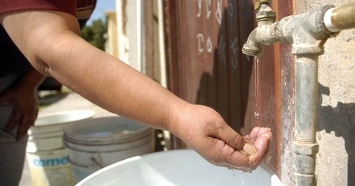Mano recolectando agua de un grifo con recipientes de plástico al fondo, representando la escasez de agua en Los Mochis.