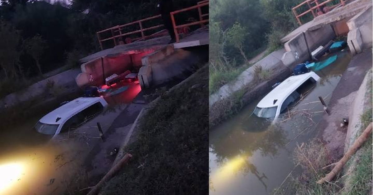 Camioneta blanca sumergida en canal de riego en El Fuerte, rodeada de vegetación y estructura de concreto.