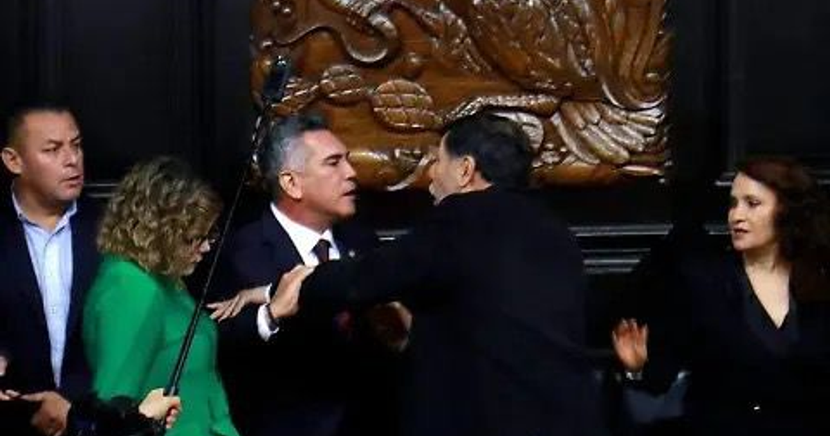 Grupo de personas en un evento político con un panel decorativo al fondo, reflejando tensiones en el Senado entre Alito Moreno y Noroña.