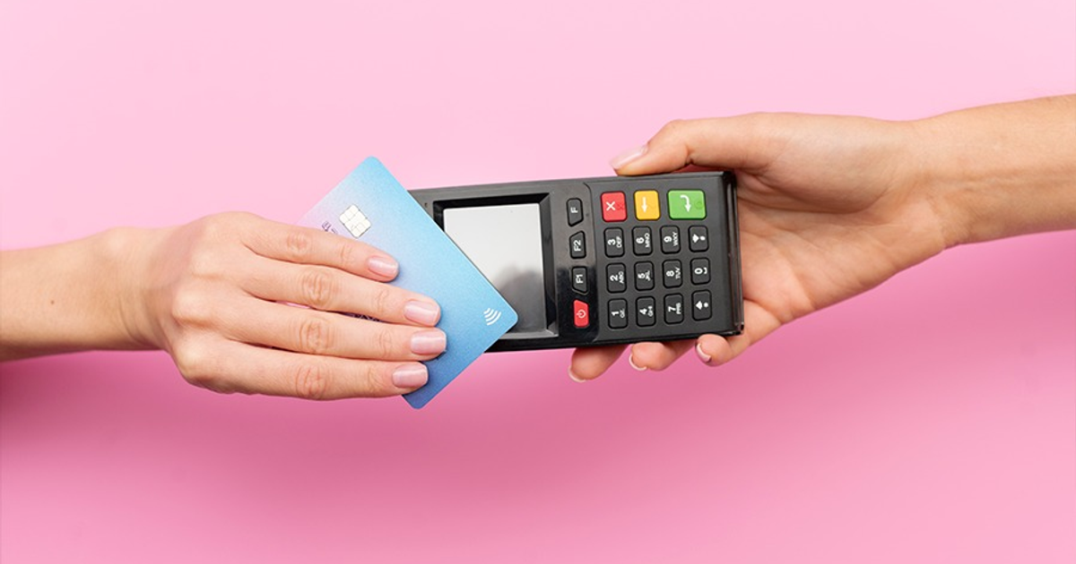 Tarjeta de crédito siendo utilizada en un terminal de pago, fondo rosa.
