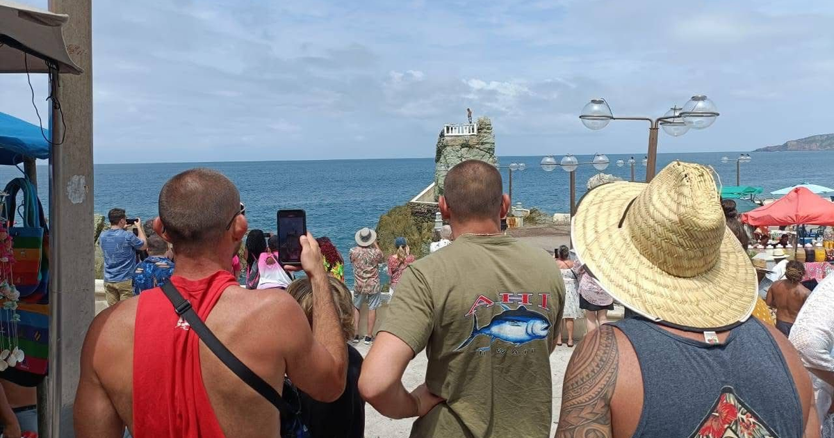 Grupo de turistas en Mazatlán observando el mar y tomando fotos, con un acantilado y sombrillas de colores al fondo.