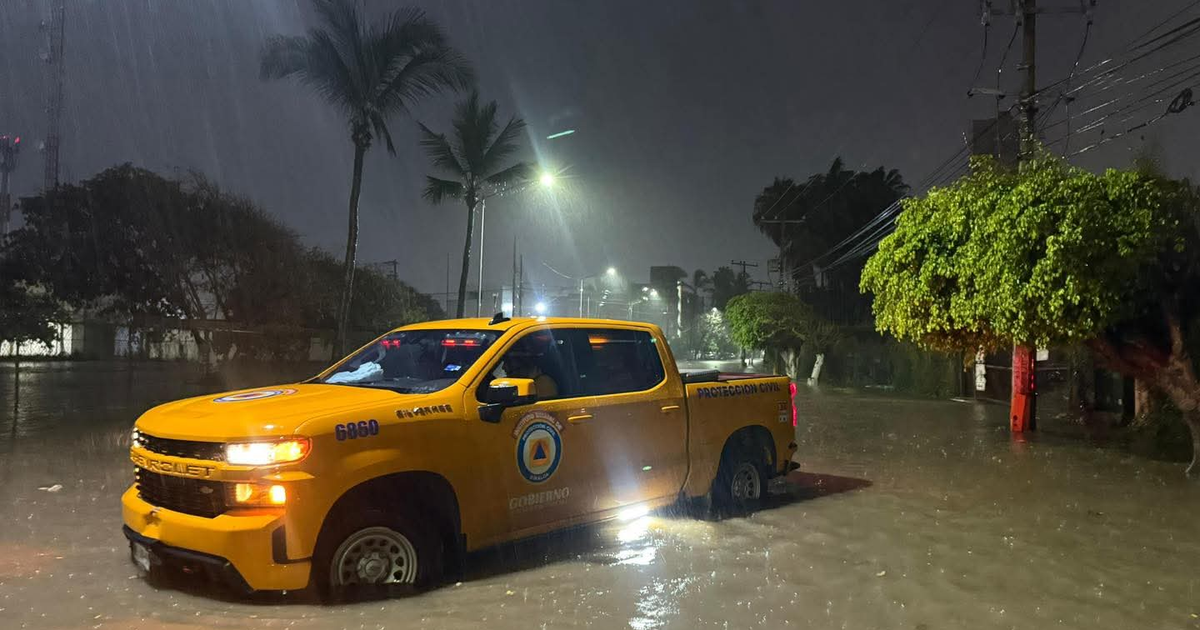 Camioneta amarilla sumergida en agua durante inundación urbana con clima lluvioso y oscuro.