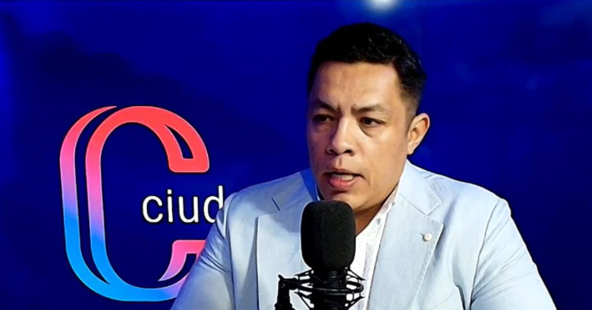 Persona hablando frente a un micrófono con fondo de ciudad y logo rojo y azul