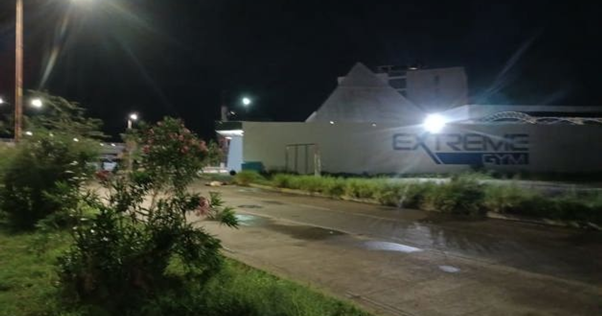 Vista nocturna de la carretera y gimnasio 'Extreme Gym' en Isla Musala, Culiacán, con iluminación de faros y luces del gimnasio.