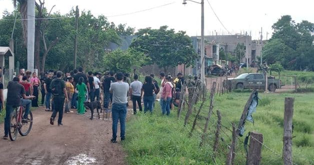 Grupo de personas en una calle de tierra en El Rosario, Sinaloa, con un perro y un vehículo al fondo.