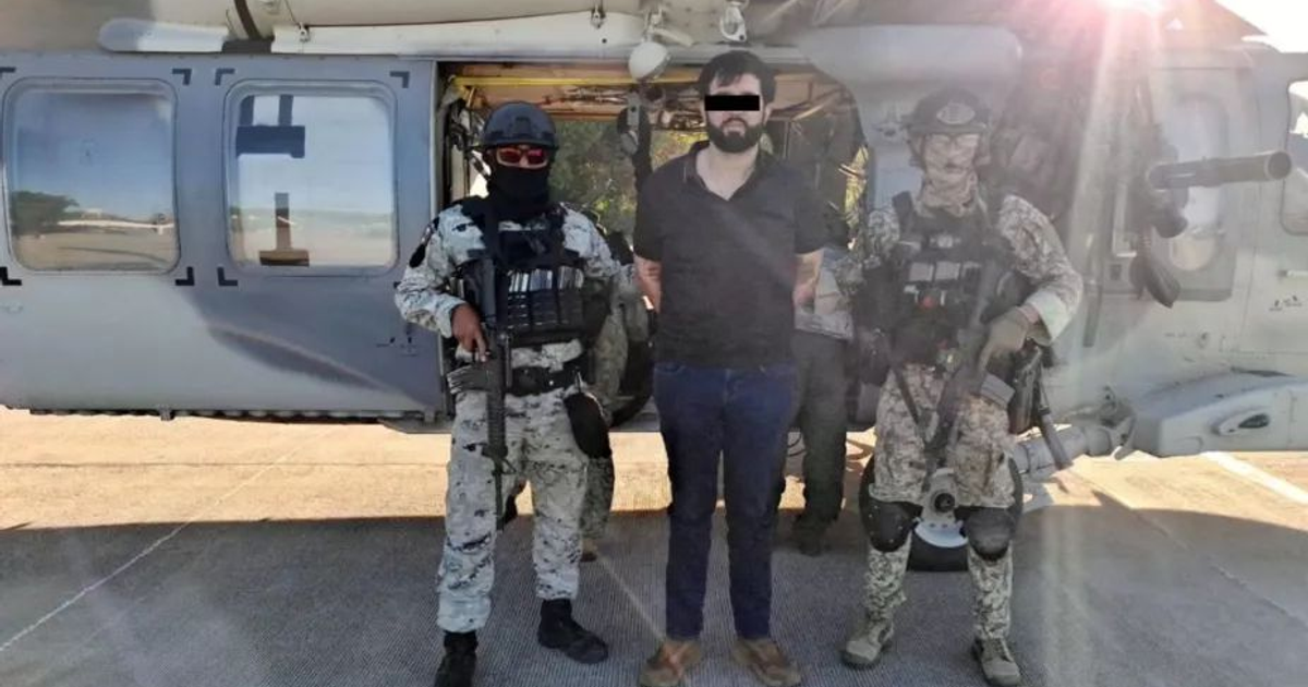 Hombre esposado escoltado por agentes armados frente a un helicóptero durante operación de extradición.