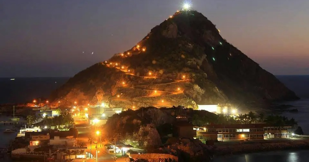 Montaña iluminada en la costa con puerto y mar al atardecer