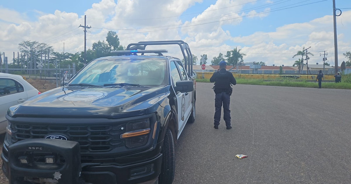 Camioneta de policía negra estacionada en una calle urbana con un oficial de espaldas en Culiacán, Sinaloa.