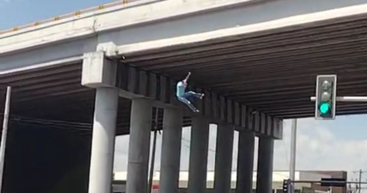 Persona colgando de un puente elevado en Gómez Palacio con semáforo en verde.