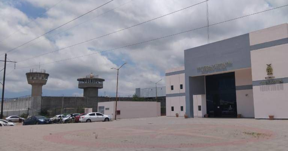 Entrada de la prisión 'El Castillo' en Mazatlán con torres de vigilancia y vehículos estacionados.