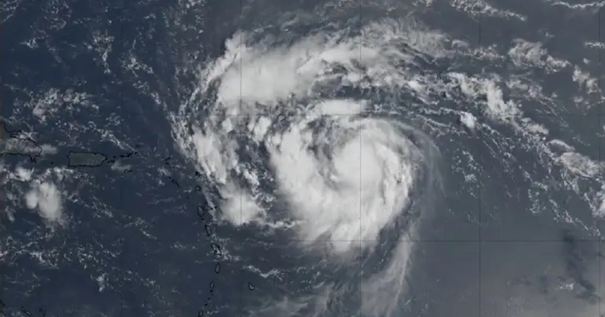 Imagen satelital del huracán Erin en el océano Atlántico, mostrando su forma espiral y nubes densas, con islas visibles a la izquierda.