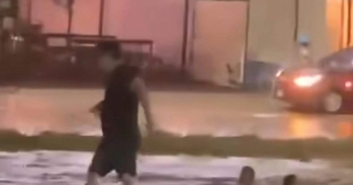 Hombre caminando en superficie mojada con automóvil y edificios al fondo, reflejando el impacto de las lluvias en Mazatlán.