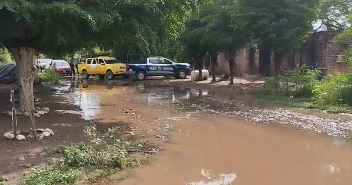 Calle inundada en Palos Blancos con vehículos estacionados, incluyendo uno de la Policía Municipal, tras una intensa lluvia.