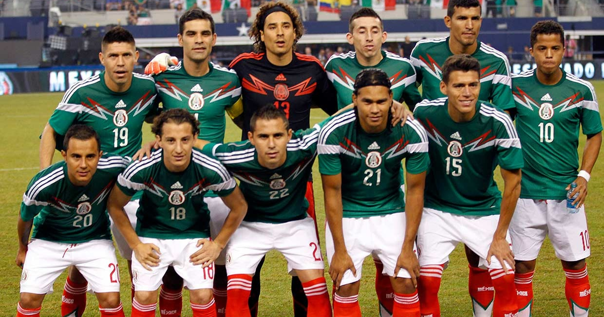 Jugadores de la selección mexicana de fútbol posando en el campo con camisetas verdes, preparándose para el amistoso contra Japón.