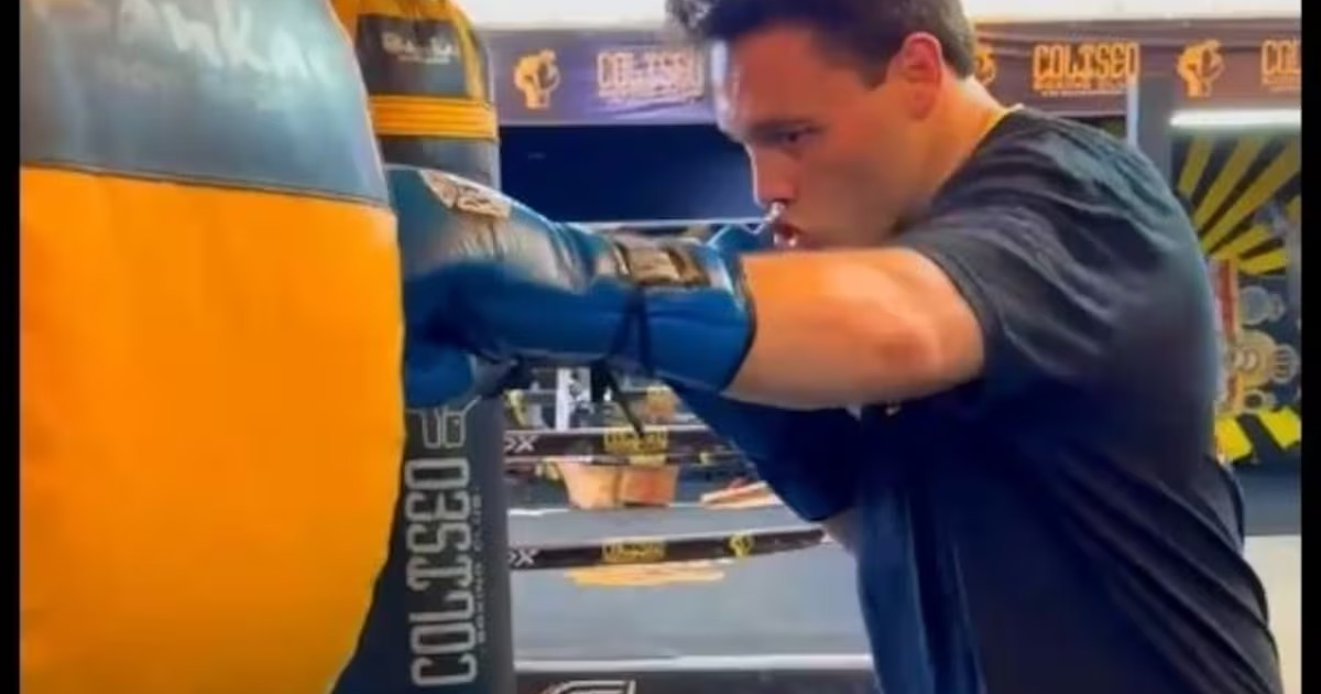 Persona entrenando con saco de boxeo en gimnasio, usando guantes azules.