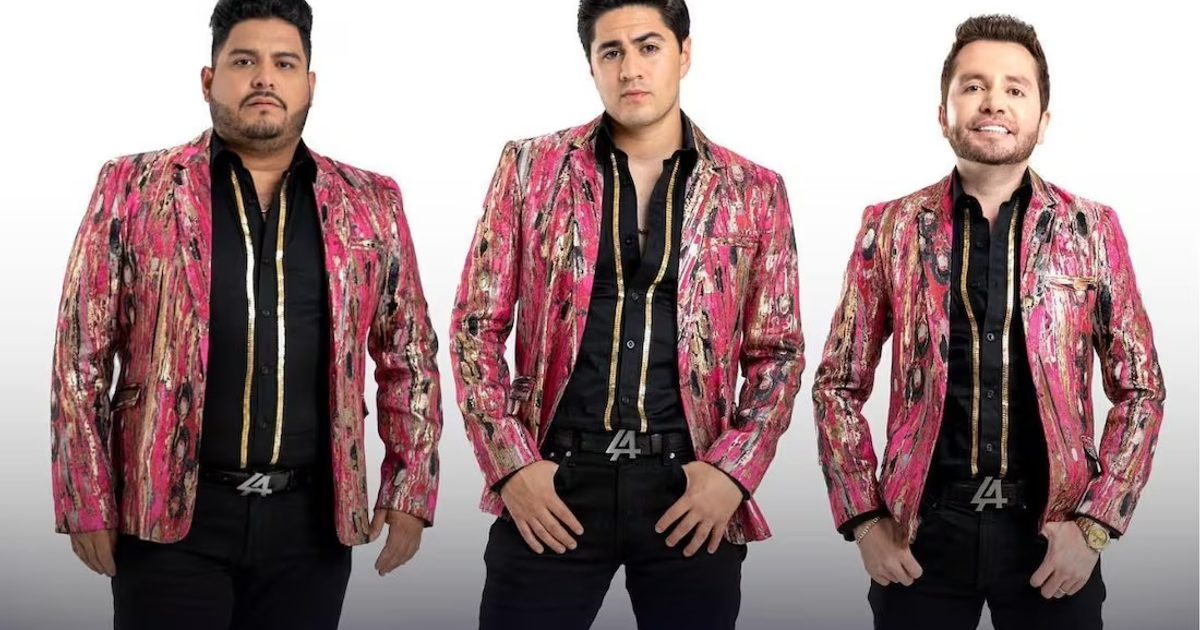 Integrantes de La Adictiva con chaquetas rosas y doradas posando frente a un fondo blanco.