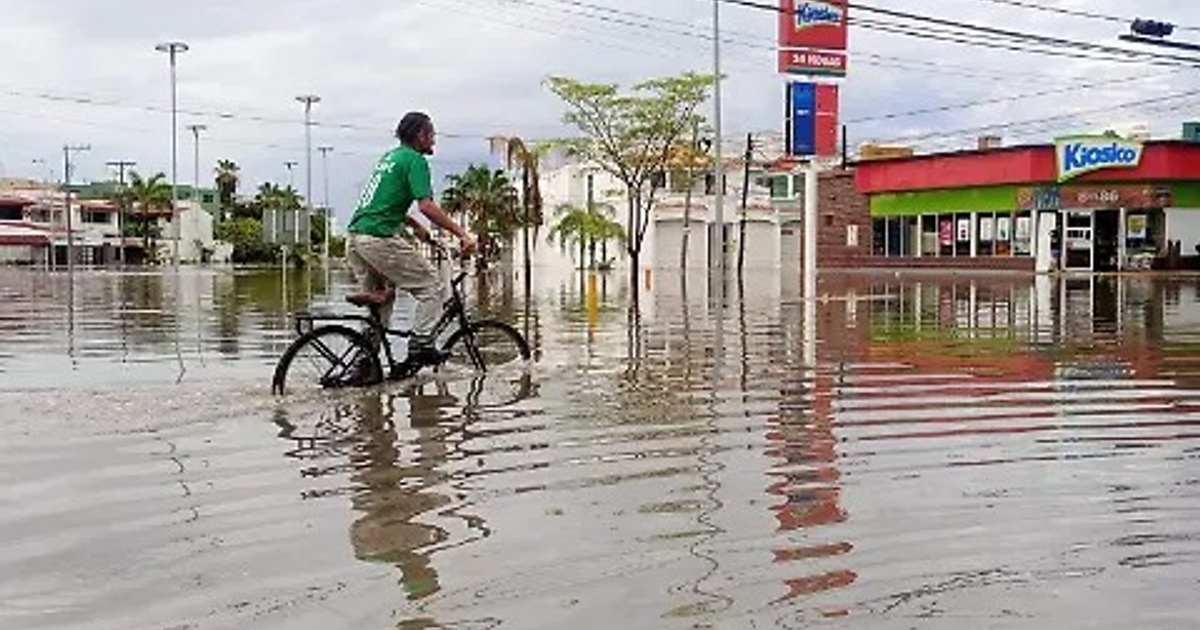 Hombre en bicicleta en calle inundada en Sinaloa, tras intensas lluvias.