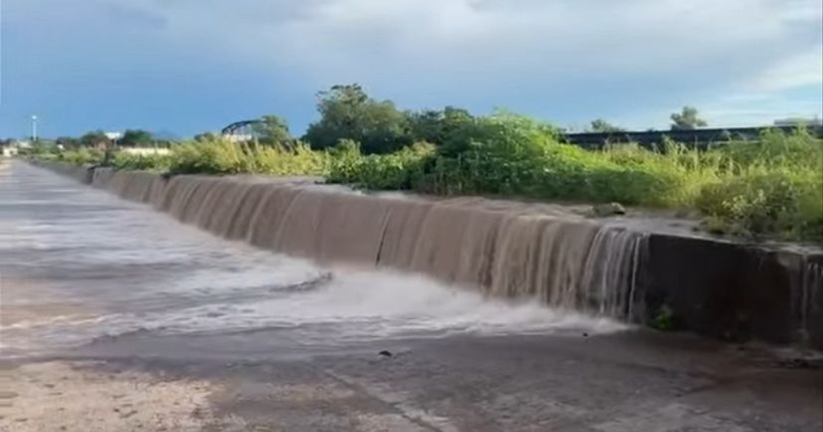 Cascada de agua en Culiacán tras lluvias intensas, rodeada de vegetación y cielo nublado.