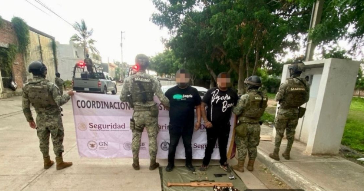 Soldados detienen a dos hombres en Mazatlán durante operativo de seguridad, con armas y pancarta de coordinación en el suelo.