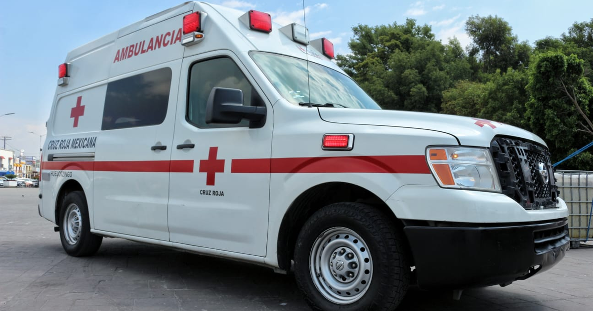Ambulancia de la Cruz Roja Mexicana estacionada en una ciudad, con edificios y árboles al fondo.