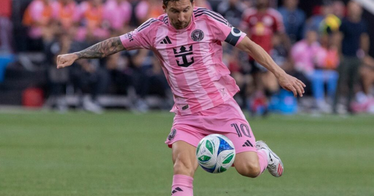 Jugador de fútbol con camiseta rosa en acción durante un partido, con balón azul y verde.