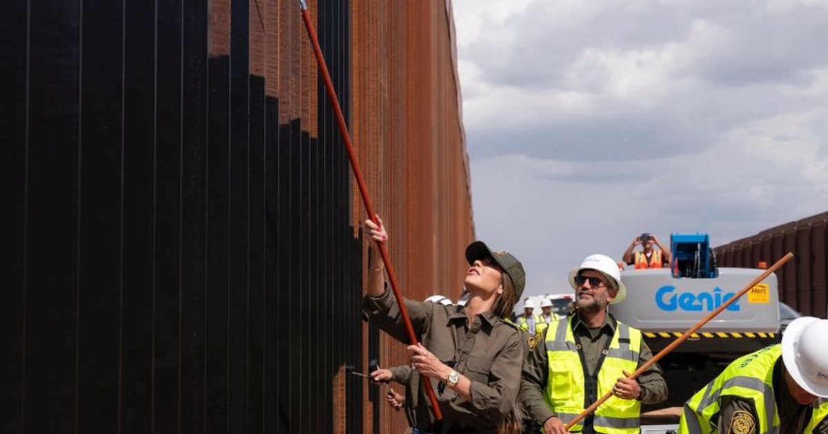 Personas pintando el muro fronterizo en El Paso, Nuevo México, con maquinaria y cielo nublado de fondo.