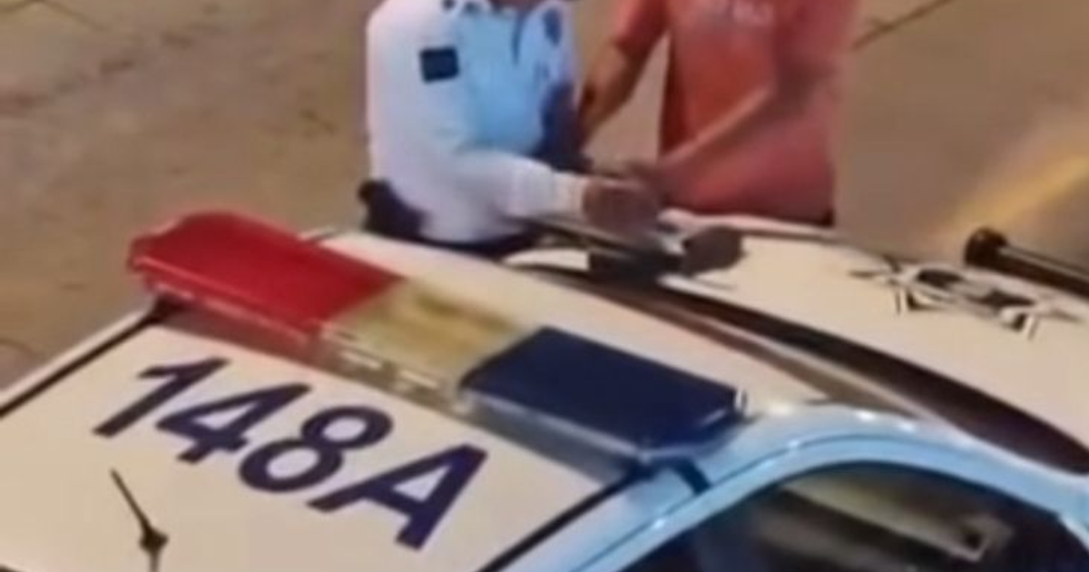 Oficial de tránsito en Mazatlán sobre el capó de un vehículo patrulla, interactuando con un conductor.