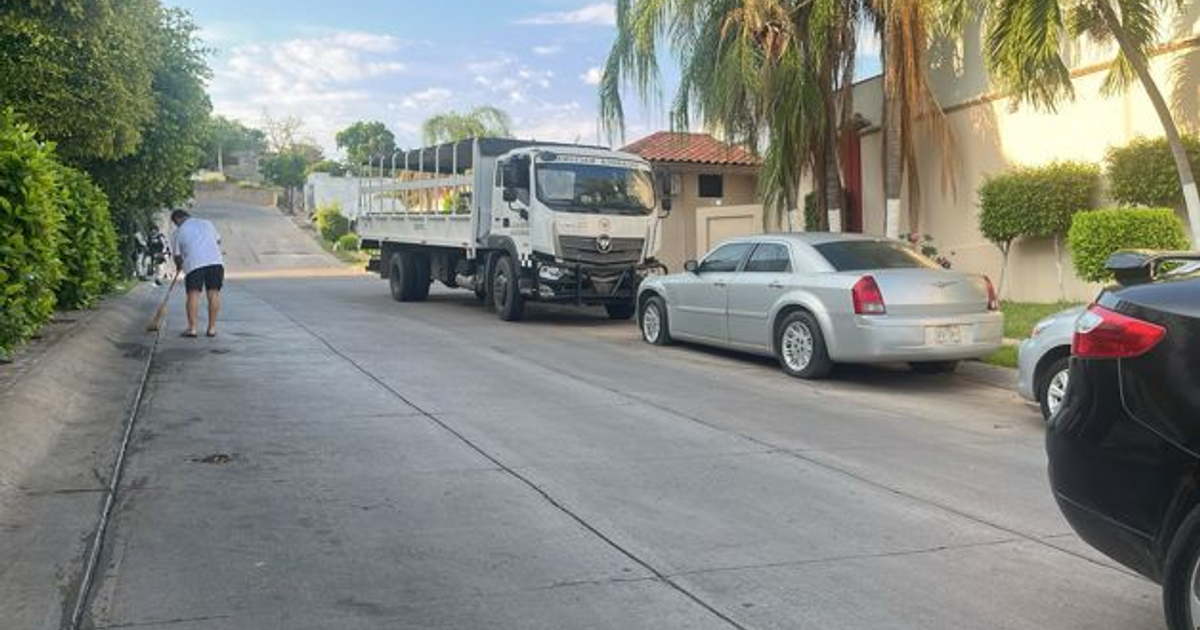 Calle residencial en Culiacán con hombre barriendo y vehículos estacionados durante operativo militar.