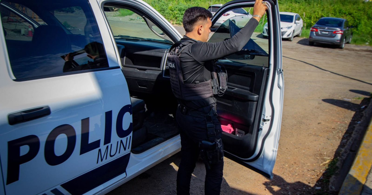 Oficial de policía inspeccionando una patrulla en un estacionamiento en Mazatlán.