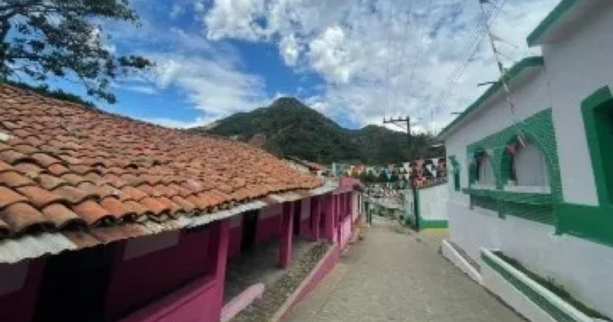 Vista de un paisaje urbano con casas de techos de teja, montaña al fondo y banderines decorativos.