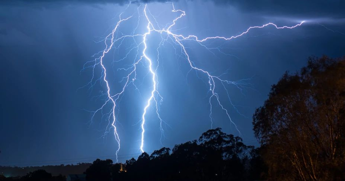 Rayos iluminan el cielo nocturno en Culiacán durante una tormenta eléctrica, con nubes oscuras y siluetas de árboles.