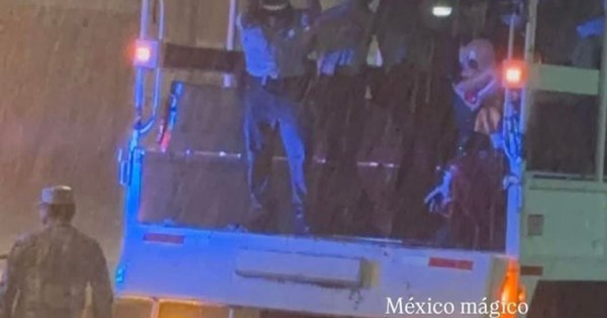 Camión de servicio público con luces intermitentes y personas, una disfrazada, en un entorno lluvioso durante el rescate de Criky Mouse en Mazatlán.