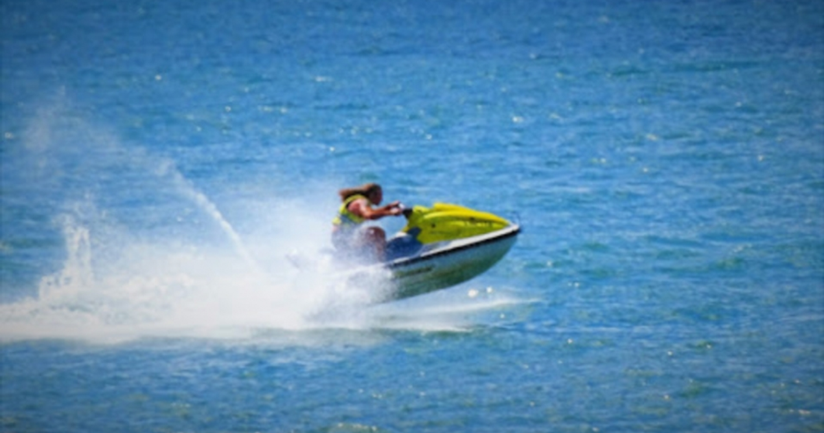 Persona montando un jet ski en movimiento sobre el agua azul de Mazatlán, salpicando agua a su paso.