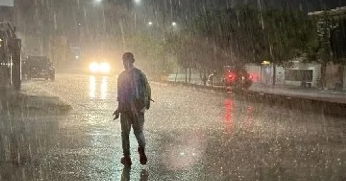 Persona caminando bajo la lluvia en una calle de Culiacán, con charcos reflejando luces de vehículos.