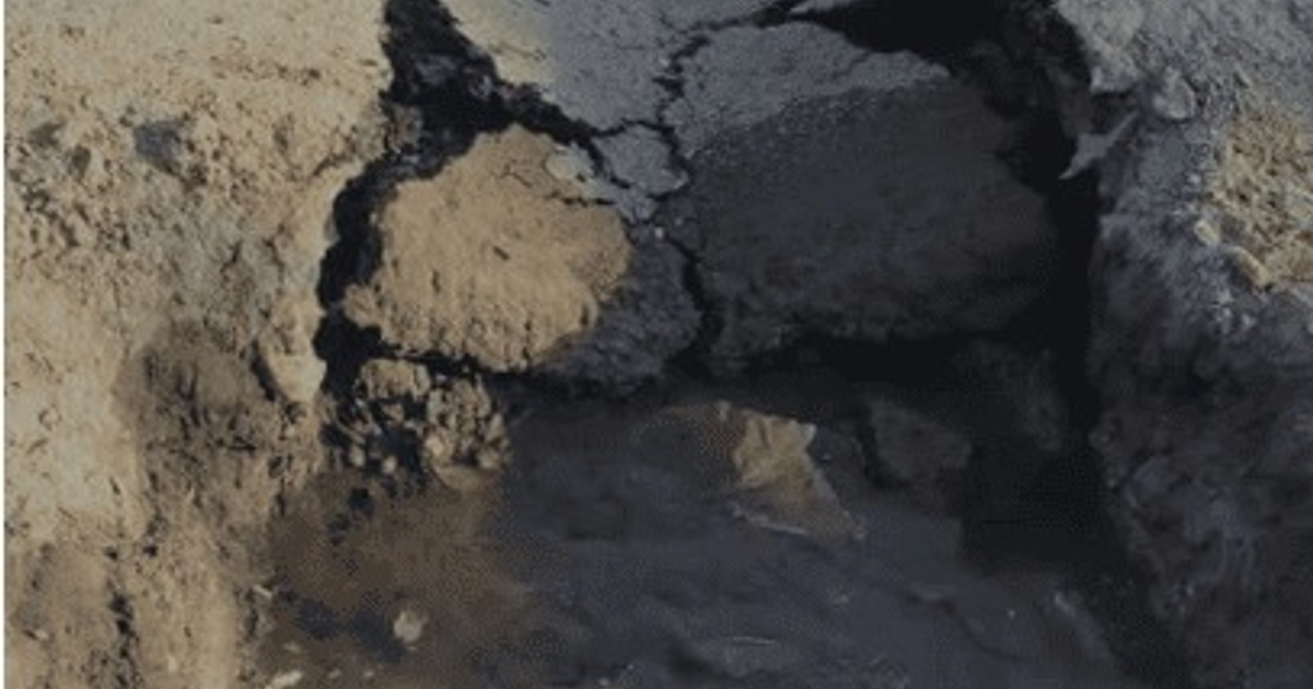 Terreno erosionado con grietas y charco de agua, posible indicativo de problemas de drenaje.