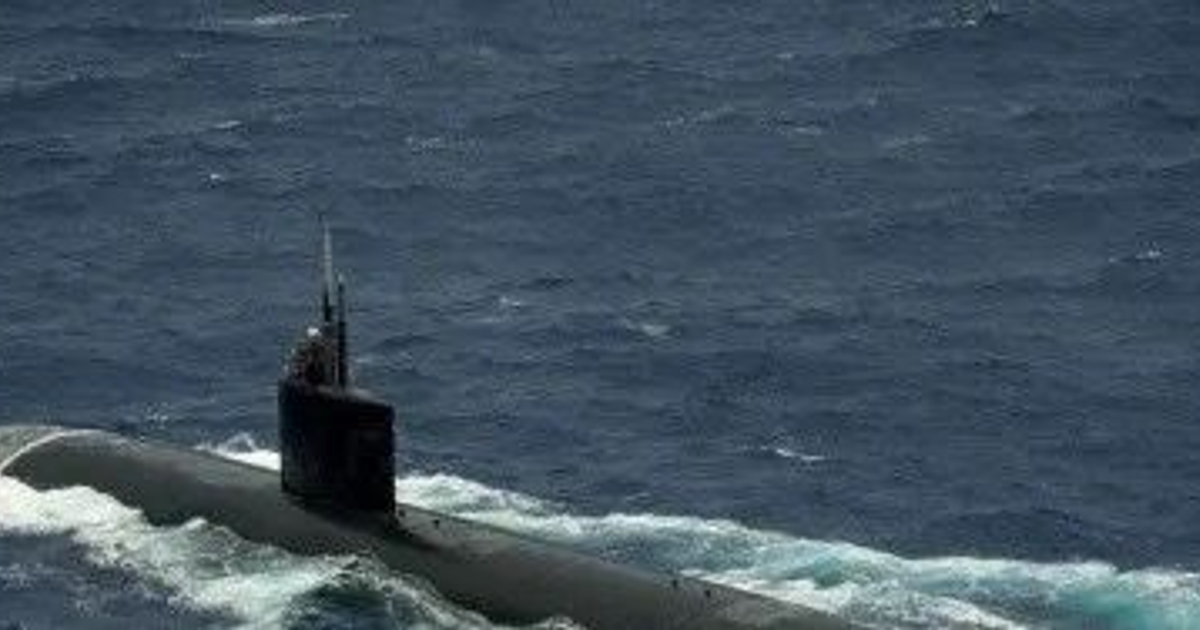 Submarino nuclear en la superficie del mar con olas alrededor, destacando su torreón visible.