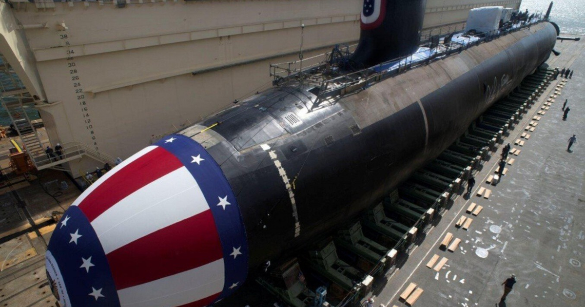 Submarino en dique seco con colores de la bandera estadounidense, rodeado de actividad en un astillero.