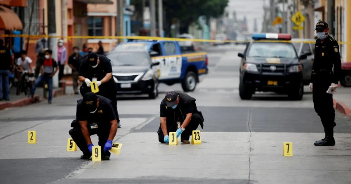 Oficiales de policía investigan una escena del crimen en México, con marcadores de evidencia y vehículos policiales al fondo.