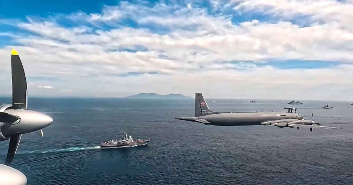 Avión militar sobre el océano con barco y nubes en el fondo