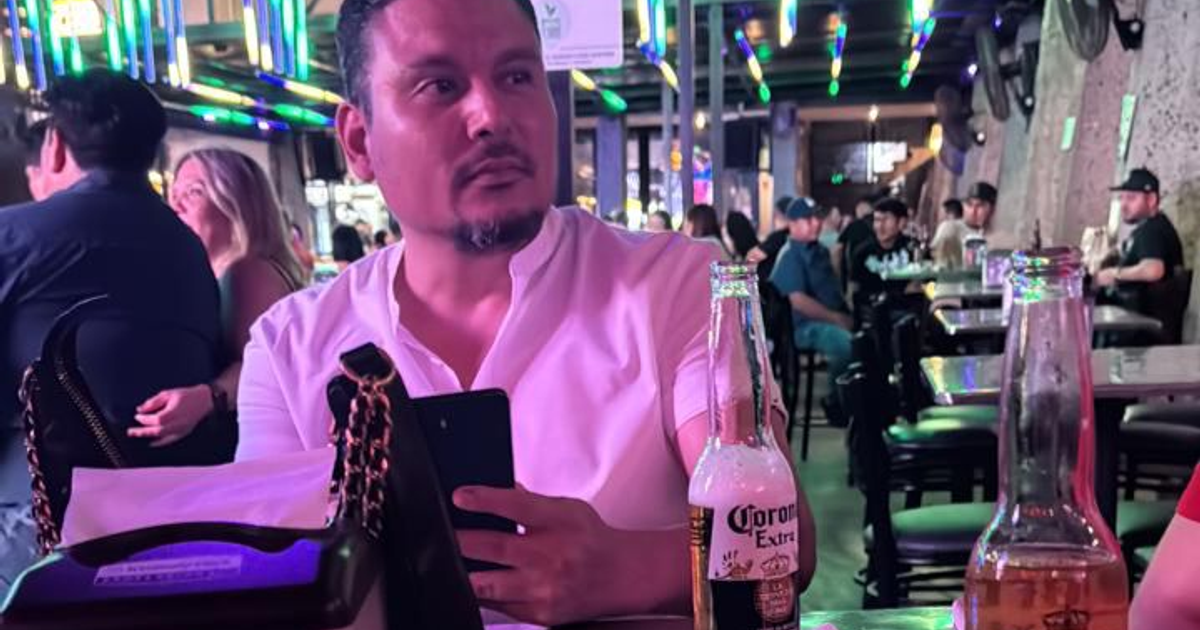 Hombre en bar con cerveza Corona Extra, ambiente colorido y concurrido.