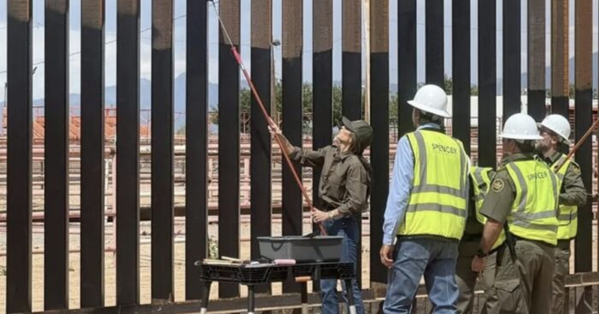 Trabajadores pintando la valla fronteriza de negro para aumentar su temperatura.