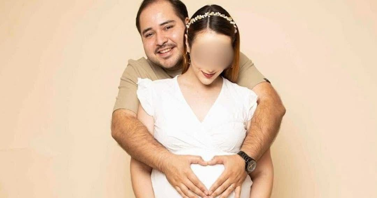 Pareja en sesión de fotografía de maternidad, el hombre abraza a la mujer embarazada formando un corazón con sus manos sobre su abdomen.