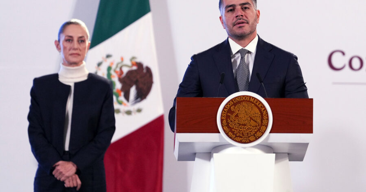 Omar García Harfuch en conferencia de prensa sobre el Cártel de Sinaloa, con bandera de México al fondo.