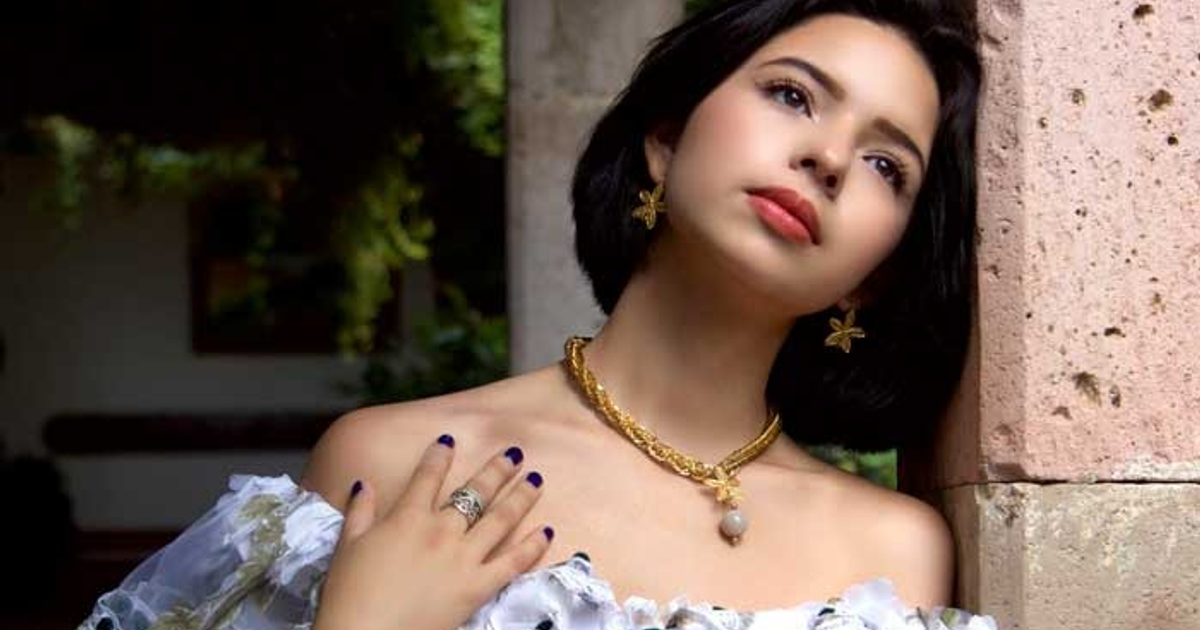 Ángela Aguilar con peinado corto, collar dorado y expresión contemplativa en un entorno natural.